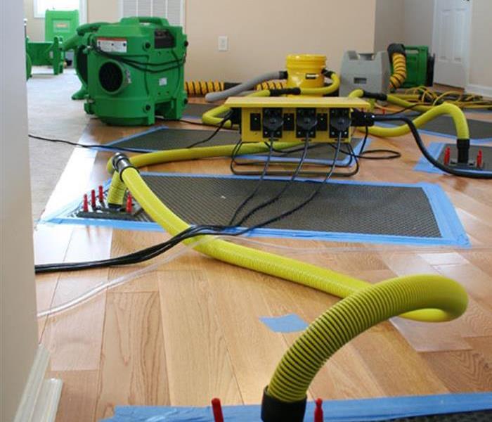Hardwood floors with a floor drying mats and yellow tubes running to the machine